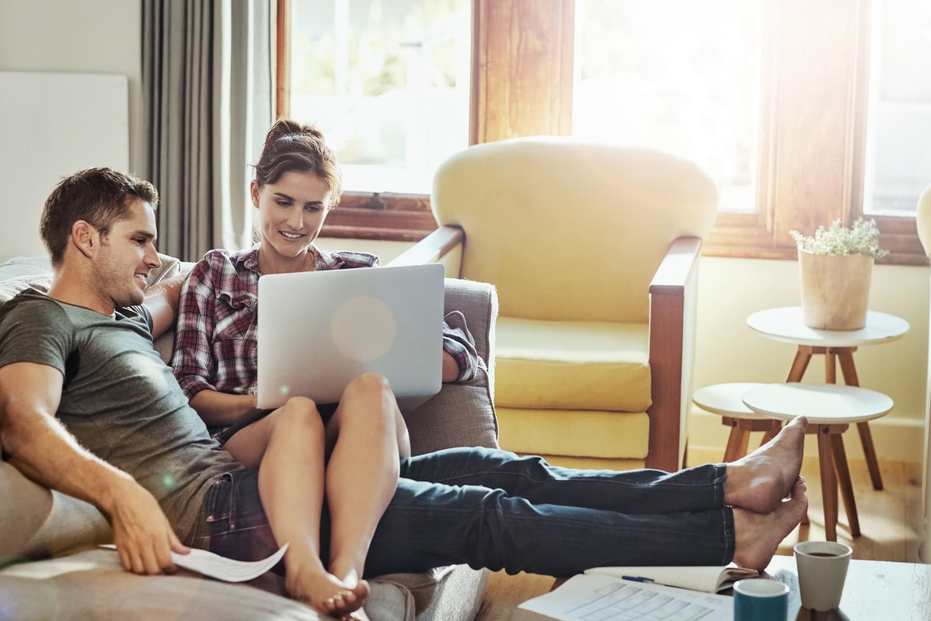 A man and a woman sitting on a couch looking at a laptop together