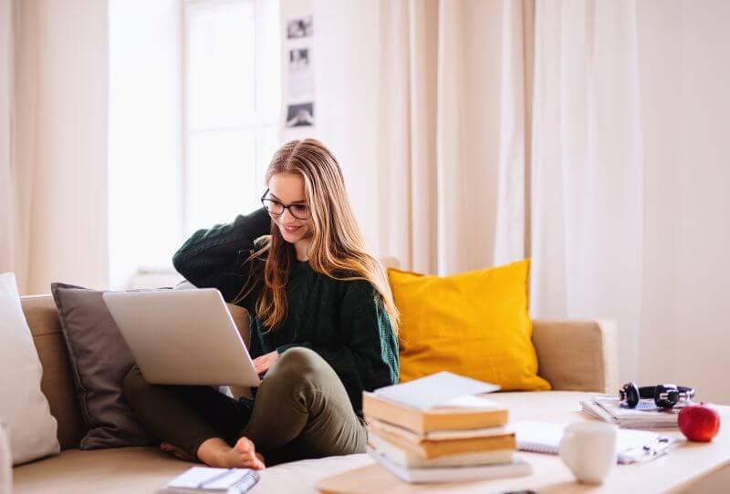 Young woman smiling at her laptop on the couch, checking her credit score before applying for a personal loan