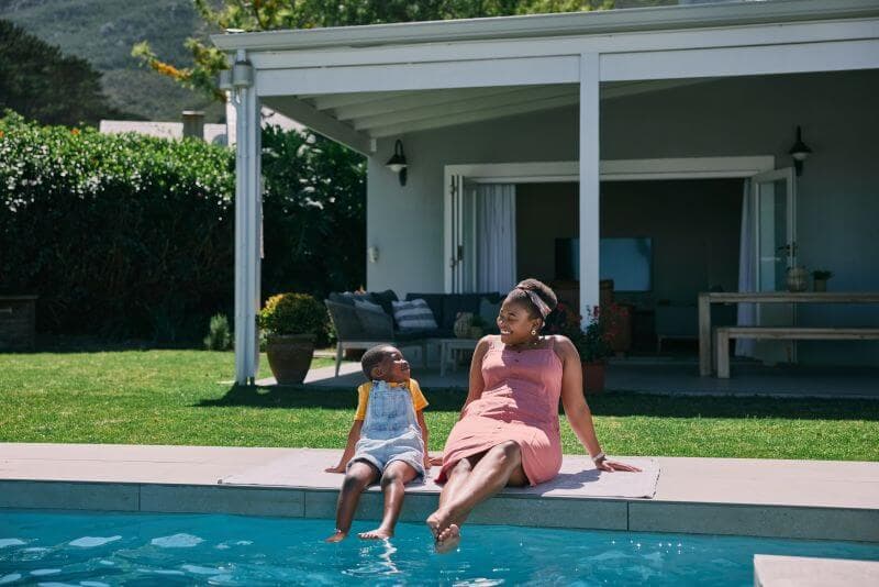 Mother and child sitting poolside at their home, feet in the water, enjoying a relaxed afternoon made possible by getting credit card debt under control