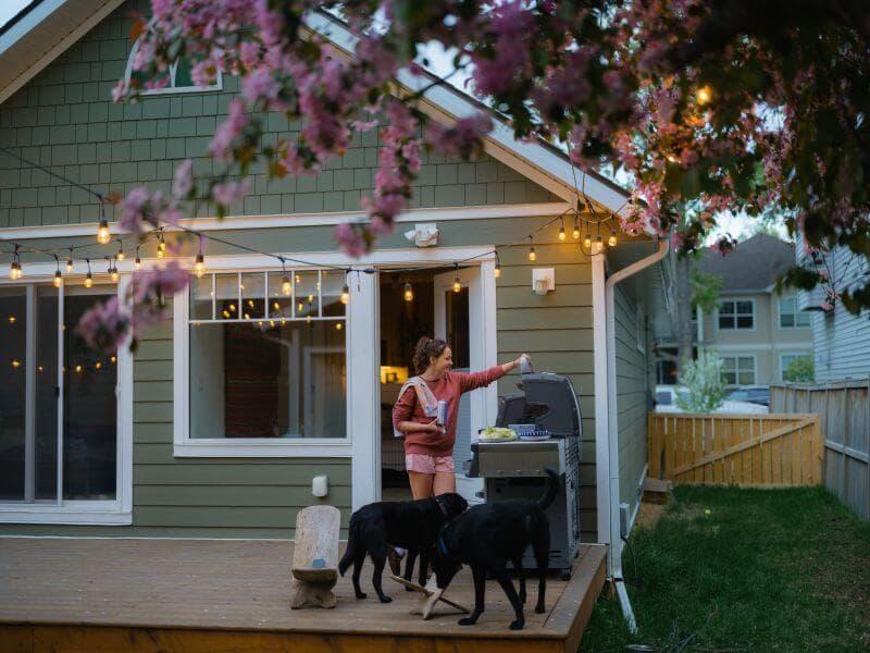 Woman grilling on her back deck at dusk with her dogs, enjoying a home with enough equity to qualify for a HELOC