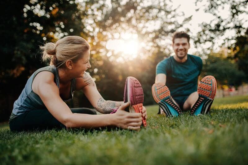 Couple stretching together in a sunny park, building healthy financial habits alongside an active lifestyle with a predictable personal loan repayment plan